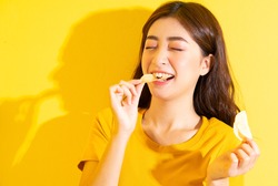 Young Asian girl eating snack on yellow background