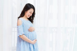 Beautiful woman holding her pregnant belly by the window