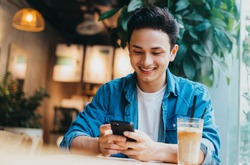 Young Asian man sitting and using smartphone at coffee shop