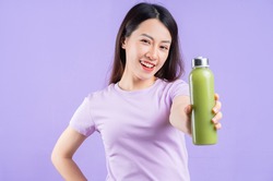 Young Asian woman holding a bottle of juice on purple background