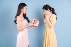 Two young Asian woman holding pink gift box on blue background