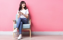 Asian woman sitting on sofa using her phone with a happy expression	