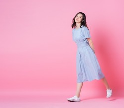 Full length image of young Asian woman wearing blue dress on pink background