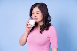 Image of middle aged Asian woman drinking milk on blue background