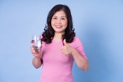 Image of middle aged Asian woman drinking water on blue background