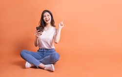 Full length image of young Asian girl using smartphone on orange background