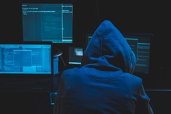 Hacker using computer for organizing massive data breach attack on goverment servers. Hacker in dark room surrounded computers