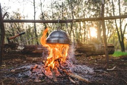 kettle is heated on a bonfire.  travel in the forest. Outdoor recreation concept. Teapot over the fire. Beautiful campfire in a tourist camp in the autumn forest with a hatchet on background
