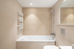 Modern bathroom with beige tiles, bathtub, shower and rectangular large mirror.