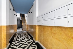 Lobby at entrance of house with long corridor, stairs to second floor, black and white marble mosaic floor, bright yellow walls, lamps in black metal lampshades and mailboxes.