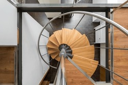Modern spiral staircase with wooden steps and metal railings looking down from above creates a feeling of weightlessness. Stylish staircase with beautiful architecture in houses with trendy design.