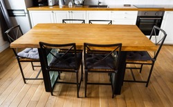 A big wooden dining table with glass blocks and metal wicker chairs and pillows in modern scandinavian an eat-in kitchen, against light wood floor, bright white furnitures and appliances