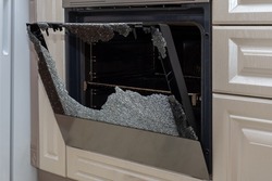 Opened broken oven door in the kitchen, side view, close-up. Broken glass from overheating. Broken glass from impact