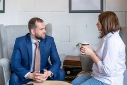 A young woman in a white shirt and jeans holding a mug of coffee and a middle-aged Arab man in a business suit talking at a cafe table. Coworking.