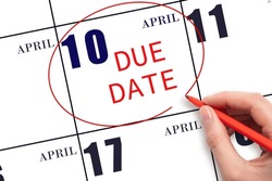 10th day of April. Hand writing text DUE DATE on calendar date April 10 and circling it. Payment due date. Business concept. Spring month, day of the year concept.