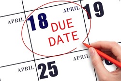 18th day of April. Hand writing text DUE DATE on calendar date April 18 and circling it. Payment due date. Business concept. Spring month, day of the year concept.