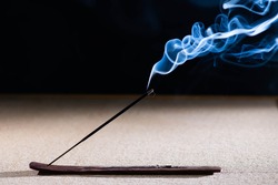 Lit incense stick with smoke on a black background