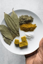 Spices for cooking meat on a white plate, curry, thyme, bay leaves, salt and stock cubes on a white plate, classic spices in Nigerian cooking