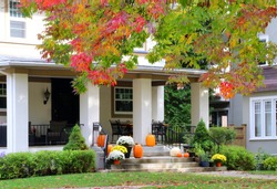 Seasonal house outdoor decoration. Main entrance stair and porch of the stylish house decorated for autumn holidays season, branches of the colorful tree on a foreground. Fall background.