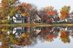 Fall cityscape with private houses neighborhood along a pond. Colorful trees and houses reflected in a water. Midwest USA, Wisconsin. Classic american middle class homes background.