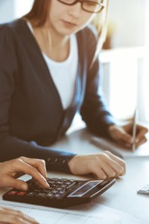 Accountant checking financial statement or counting by calculator income for tax form, hands close-up. Business woman sitting and working with colleague at the desk in office. Audit concept