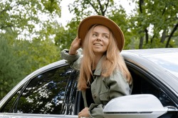 Blonde woman in hat sticking head out of windshield car. Young tourist explore local travel making candid real moments. True emotions expressions of getting away and refresh on open clean air