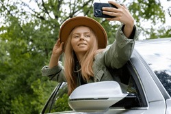 Blonde woman stoped car on road to take a selfie photo. Young tourist explore local travel making candid real moments. True emotions expressions of getting away and refresh on open air