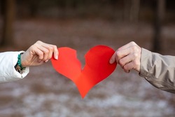 Two hands, male and female, tear red heart symbol of lovers against background of winter forest. Сoncept of breaking up relationship. Love is over. Resentment and separation. Negative.