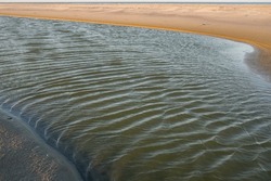 thin pool of sea water trapped on a sand bar after the outgoing low tide left marine life stranded in this tidal water feature along the coastal ecosystem