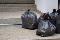 Pile of black plastic bags that contains garbage inside on the floor. Waiting for the rubbish keeper officers to take them away. Concept : Waste management. Collected for disposal.  