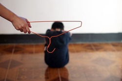 Hand holds cloth hanger to punish a guilty feeling boy sit on the floor. Concept : Intimidation or stick discipline strategy to control or punish kid behavior that affect to mental in childhood. 