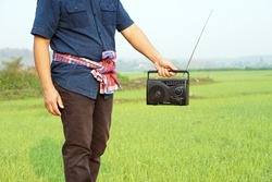 Farmer holds FM-AM radio receiver at paddy field. Concept : Happy working along with music. Country lifestyle. Getting knowledge, information , news , advertisement, songs from listen to radio.     