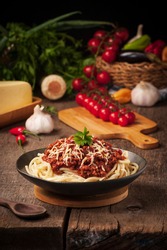 spaghetti bolognese served in a dark dish on a rustic wooden table. Blurred background with spaghetti ingredients