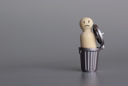 Wooden doll inside trash can. Down in the dumps, depressed, sad and miserable concept. Copy space