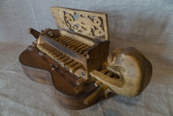 Folk antique musical instrument hurdy-gurdy handmade of wood with an open carved keyboard cover and a fingerboard  in the form of a dragon's head on a gray linen canvas