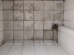 Close-up of a dirty white tile bathroom floor with a floor drain at the corner