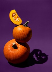Dark artistic photo of orange pumpkins on purple background. Shadow as Jack head. Balancing vegetables. Halloween concept. Hard light food photography