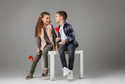 happy smiling stylish little couple child girl and boy with red hearts on stick in fashionable clothes sittting together at studio. St. Valentine's Day.