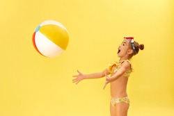 cute little child girl in swimwear playing with beach ball on yellow background