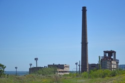 Remains of an old industrial plant or factory. A pile of stones, bricks and debris overgrown with plants, in the center a tall brick chimney