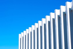 Fence on the sky background. Abstract walls and architecture against the blue sky with clear and beautiful shadows. Modern concept.