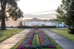 Two pathways with flower gardens between them lead to a view of the American Falls section of Niagara Falls.  View of both Canada in the foreground and the United States in the background.