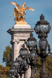 Gold, Gilded winged horse (Fames) on column with lamp posts and trees on