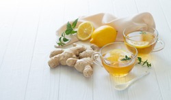 Two cups of healthy ginger tea with mint leaves and lemon on white table. Space for your text