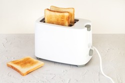 Sliced hot toasted bread for breakfast in modern white toaster on home kitchen table