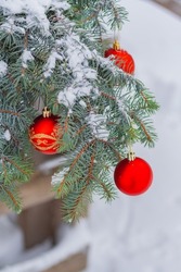 red christmas baubles hang on snowy fir branches outdoor. festive street decor.