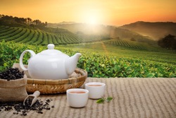 Warm cup of tea with teapot, green tea leaves and dried herbs on the bamboo mat at morning in plantations background with empty space, Organic product from the nature for healthy with traditional