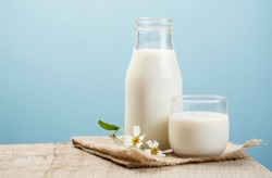 A bottle of milk and glass of milk on a wooden table on a blue background