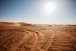 Desert scenic landscape of orange sand with vehicle traces and setting sun, wild nature of Dubai, UAE