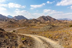 Copper Hike trail, winding gravel dirt road through Wadi Ghargur riverbed and rocky limestone Hajar Mountains in Hatta, United Arab Emirates. 